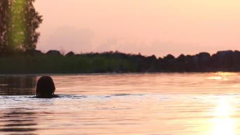 Female-swimmer-in-lake-at-sunset,-slow-motion