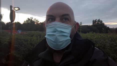 Male-in-workplace-wearing-uniform-adjusts-PPE-face-mask-against-corona-virus-at-sunrise