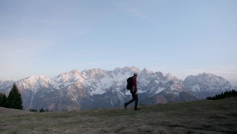A-man-with-a-backpack-wearing-a-red-jumper-walking-from-left-to-right-with-the-Triglav-National-Park-and-Julian-alps-in-the-background