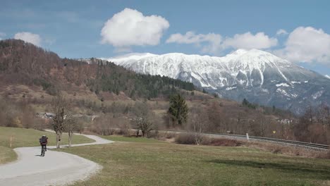 Riding-a-bike-away-from-the-camera-in-the-winter-down-a-windy-road-in-Slovenia-with-Stol-mountain-in-the-background