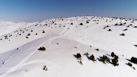 Hermoso-Vuelo-Sobre-La-Cordillera-De-Akoura-Cubierta-De-Nieve-Con-Pistas-De-Motos-De-Nieve-Y-Afloramientos-Esporádicos-De-árboles-Verdes,-Enfoque-Aéreo-Aéreo-Del-Líbano