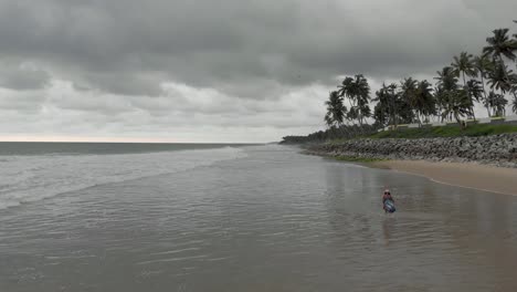4K-Luftdrohnenaufnahme-Eines-Hübschen-27-jährigen-Indischen-Mädchens,-Das-Ihren-Friedlichen-Spaziergang-Am-Strand-Genießt,-Wobei-Der-Hintergrund-Von-Regnerischen-Wolken-Entlang-Der-Küste-Von-Varkala-Bedeckt-Ist