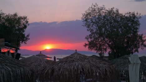 Beautiful-sunset-at-Agkistri-island,-Argosaronikos,-Greece,-with-natural-umbrellas-made-from-hay-in-the-foreground