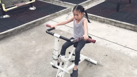 Asian-child-girl-is-exercising-with-a-machine-in-public-park-in-Bangkok,-Thailand