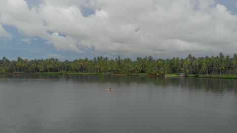 4K-Luftdrohnenaufnahme-Eines-28-jährigen-Indischen-Mannes,-Der-Ein-Kajak-Mit-Sicherheitsausrüstung-In-Den-Backwaters-Von-Varkala-Paddelt,-Umgeben-Von-Kokosnussbäumen,-Kerala