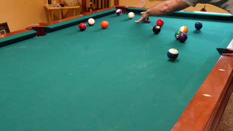 Man-Playing-8-Ball-Pool-Shoots-Several-Striped-Balls-into-Pockets-on-a-Brunswick-Table-for-Billiards-with-Green-Felt-in-Basement-of-Home,-Open-Bridge-Hand-and-Wooden-Cue-Stick,-Wide-Angle-No-Faces