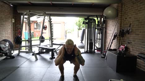 Tattooed-man-in-home-gym-front-shot-doing-squat-jumps
