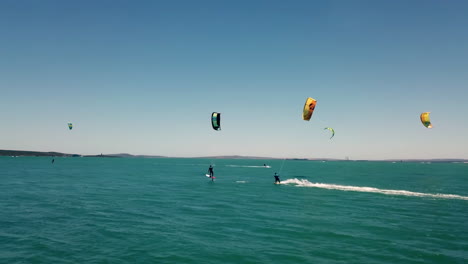 Professionelle-Wassersport-kitesurfer,-Die-Bei-Schönem-Natürlichem-Tageslicht-Mit-Blauem-Himmel-Und-Türkisfarbenem-Wasser-Auf-Dem-Offenen-Meer-In-Kapstadt,-Südafrika,-Von-Drohne-Gejagt-Werden