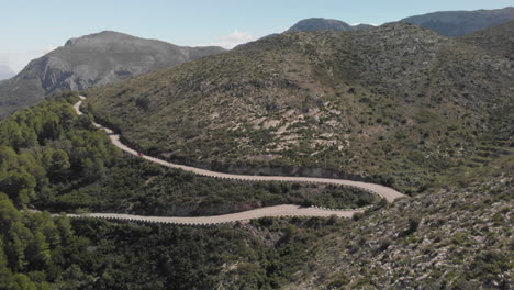 Aerial-wide-shot-red-car-drives-through-paved-road-mountain-turns-tracking-shot