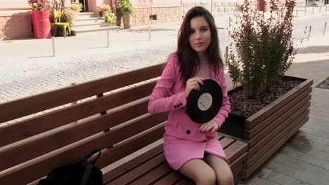 Pretty-brunette-in-pink-sitting-on-a-bench-with-a-disk-in-the-city