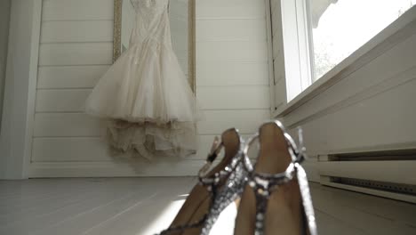 Slow-motion-pan-capturing-a-beautiful-bridal-gown-and-a-pair-of-elegant-crystal-high-heals-in-a-well-lit-sunny-white-room-at-Le-Belvédère-in-Wakefield,-Quebec,-Canada