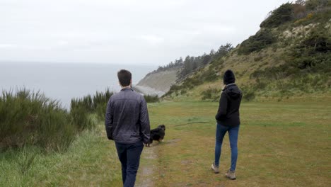 Man-and-woman-walk-near-the-ocean-with-their-dog