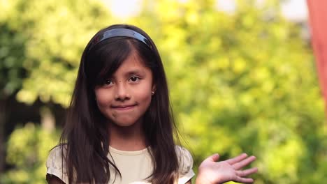 Niña-De-8-Años-Saludando-Con-La-Mano-En-El-Fondo-Verde-Del-Bokeh