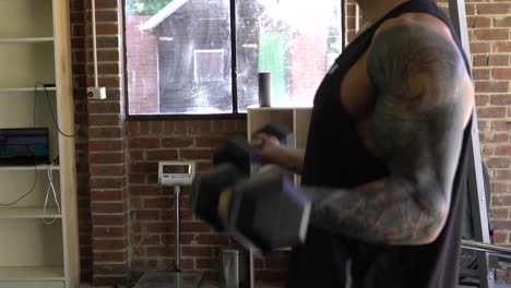 Muscly-man-with-tattoos-in-home-gym-exercising-bicep-curls-shot-from-side-blurry-shot