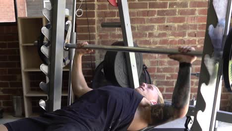 Muscly-man-in-home-gym-exercising-smith-machine-bench-press