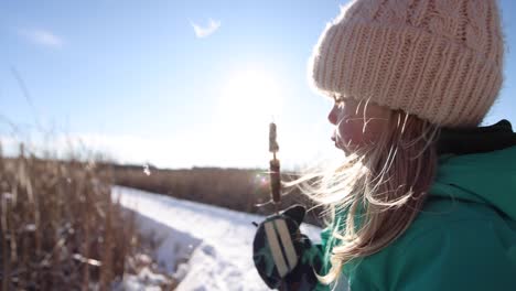 Cute-little-girl-learning-to-blow-on-cat-tail-on-winter-nature-walk-sunny-slomo