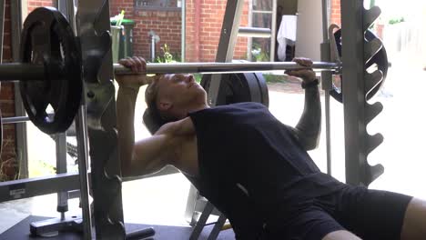 Muscly-man-in-home-gym-exercising-dooing-incline-barbell-bench-press-shot-from-front