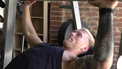 Muscly-man-in-home-gym-exercising-smith-machine-barbell-chest-press