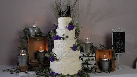 Tiered-wedding-cake-with-purple-flowers-set-up-in-front-of-a-vintage-wood-and-candle-display-at-a-wedding-reception-at-Le-Belvédère-in-Wakefield,-Quebec,-Canada