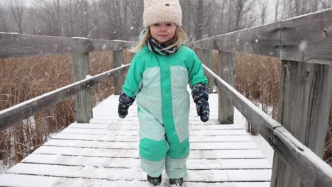 Little-girl-running-on-nature-boardwalk-in-winter-slow-motion-snow-falling