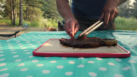Caucasian-Male-Cutting-Up-Grilled-Beef-Steak-at-Campsite