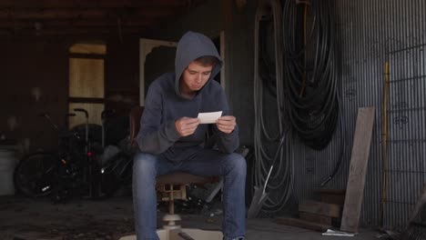A-teenage-boy-sits-alone-in-a-dirty-garage-looking-at-a-photograph