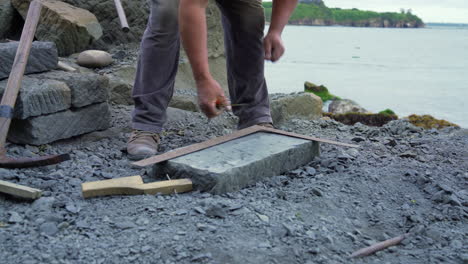 Handheld-shot-of-a-cancagua-stone-craftsman,-measuring-a-stone-slab-on-the-shoreline-of-Ancud,-Chiloe-Island