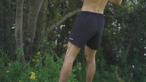 Young-caucasian-fit-attractive-male-exersicing-outdoors-Trx-back-row-exercice-with-green-vegetation-background-slow-motion