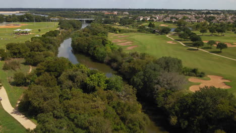 Aerial-view-of-Central-Texas-community,-trails,-real-estate,-neighborhood,-park,-shot-dives-from-high-above-trees-to-low-glide-on-river,-drone-4K