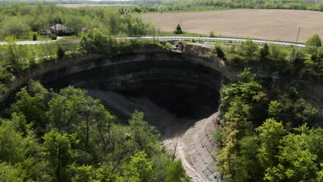 Aerial-backwards-shot-of-famous-Devil's-Punch-Bowl-surrounded-by-farm-fields-during-summer-in-Canada
