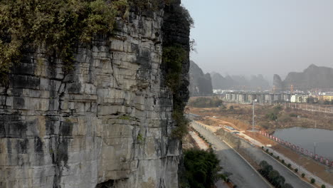 Rock-climber-ascending-karst-mountain-cliff-outside-Yangshuo-city,-China,-aerial