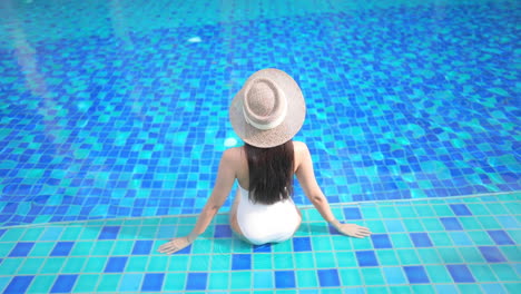 Back-of-Exotic-Sexy-Woman-in-White-Swimsuit-and-Floppy-Hat-Sitting-on-a-Swimming-Pool-Border,-Fashion-Concept,-Full-Frame