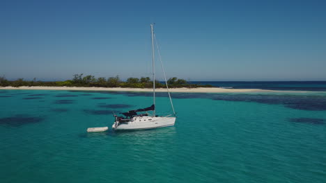 Low-close-aerial-parallax-around-sailboat-anchored-near-small-island,-Isle-of-Pines