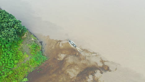 Drone-shot-following-a-small-boat-traveling-along-the-Amazon-river-bank-in-Peru