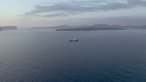 Aerial:-Panoramic-shot-of-cargo-ship-in-Santorini,-Greece-during-dusk