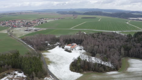 Farm-with-snow-covered-field-near-village-in-czech-countryside,-drone