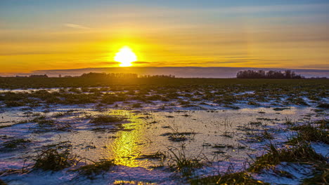 Zeitrafferaufnahme-Von-Schneebedecktem-Und-Frostigem-Ackerland-Mit-Epischem-Goldenem-Sonnenuntergang-Am-Horizont