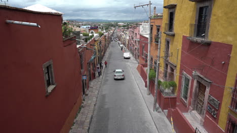 A-street-in-San-Miguel-de-Allende,-Guanajuato-Mexico-with-yellow-and-red-houses,-some-cars-and-people