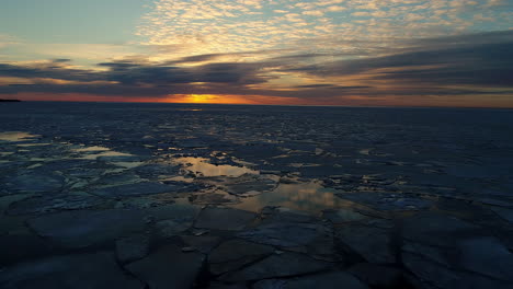 Aerial-flyover-Baltic-Sea-with-swimming-Ice-Floes-on-Water-Surface-during-sunset-at-horizon