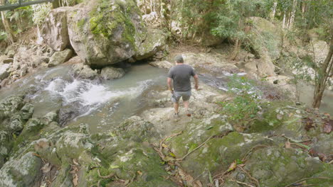 Middle-aged-man-climbs-down-rocks-to-fast-flowing-creek