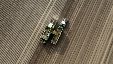 Top-down-or-birds-eye-view-onto-green-tractor-harvesting-on-brown-field-4K