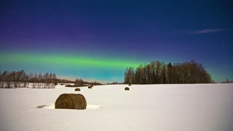 Green-shimmer-time-lapse-of-northern-lights,-snow-on-farm-land-at-full-moon