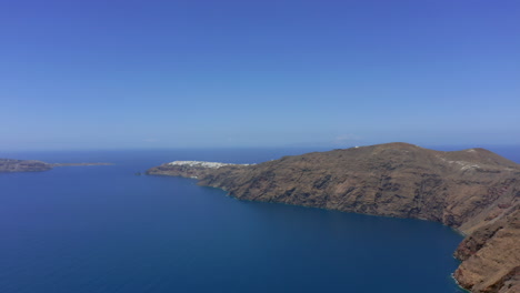 Slow-panning-panoramic-drone-shot-of-Oia-in-Santorini,-Greece-on-a-sunny-day
