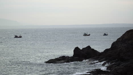 Morgennebeliger-Blick-Auf-Einen-Felsigen-Strand-Mit-Altem-Traditionellem-Fischerboot,-Das-In-Einiger-Entfernung-Auf-Der-Halbinsel-Muine,-Vietnam,-Unterwegs-Ist