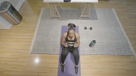 An-overhead-shot-of-a-black-female-doing-sit-ups-with-weights-in-her-hand-on-the-floor-of-her-kitchen