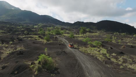 All-wheel-drive-jeep-traveling-through-black-sand-volcanic-landscape-below-volcano