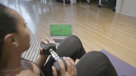 Ein-Standbild-Einer-Schwarzen-Frau,-Die-Sit-Ups-Mit-Gewichten-In-Der-Hand-Macht,-Während-Sie-Zu-Hause-In-Ihrer-Küche-Einen-Grünen-Bildschirm-Auf-Ihrem-Computer-Laptop-Betrachtet