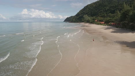 Low-angle-aerial-drone-shot-of-tropical-beach-with-man-running-on-Koh-Chang-Island-in-Thailand
