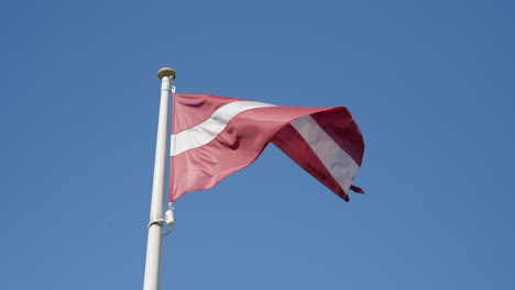 Latvian-flag-on-pole,-sunny-day