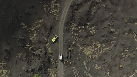 Jeep-4x4-vehicle-driving-through-dry-volcanic-sand-landscape,-aerial